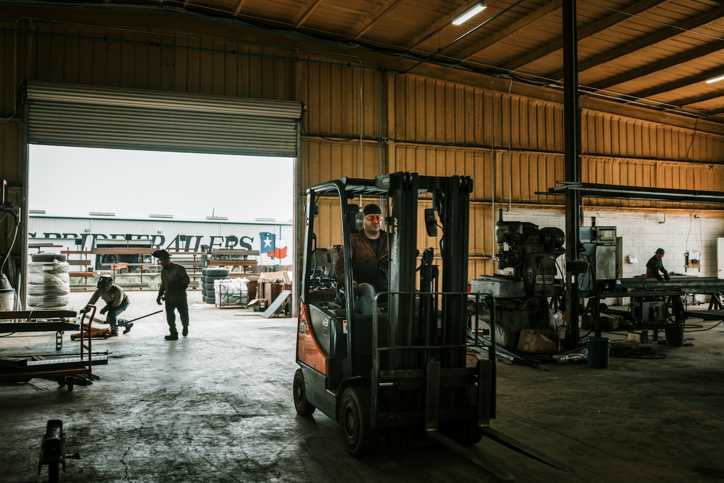 Man operates forklift in busy warehouse with workers in background.
