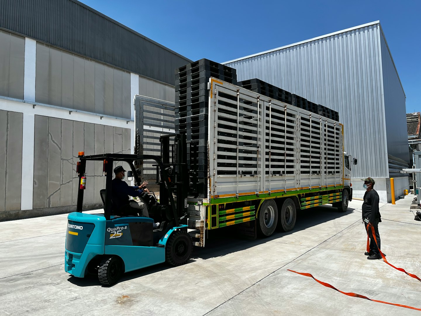 Worker drives teal forklift loading pallets onto a truck.